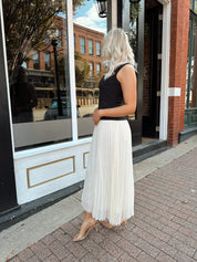 Woman wearing contrast midi dress with black top and cream pleated skirt. 
