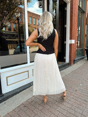 Woman wearing contrast midi dress with black top and cream pleated skirt. 