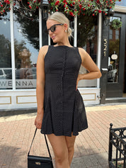 Woman wearing black polka dot mini dress with black blazer over top.