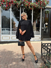 Woman wearing black polka dot mini dress with black blazer over top.