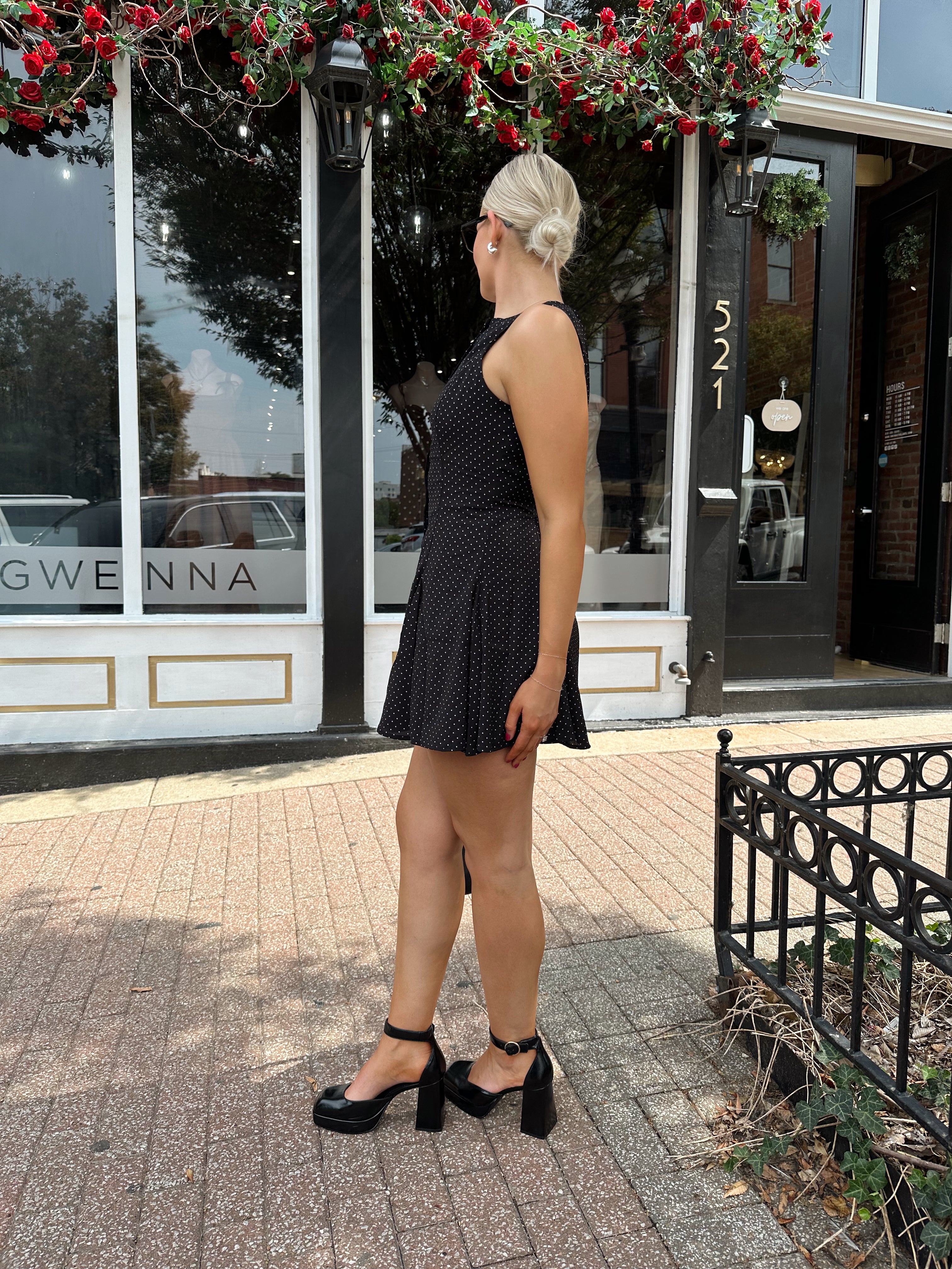 Woman wearing black polka dot mini dress with black blazer over top.