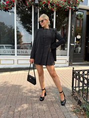Woman wearing black polka dot mini dress with black blazer over top.