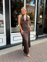 Woman wearing chocolate brown satin maxi dress with open back and long ties. 
