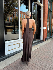 Woman wearing chocolate brown satin maxi dress with open back and long ties. 