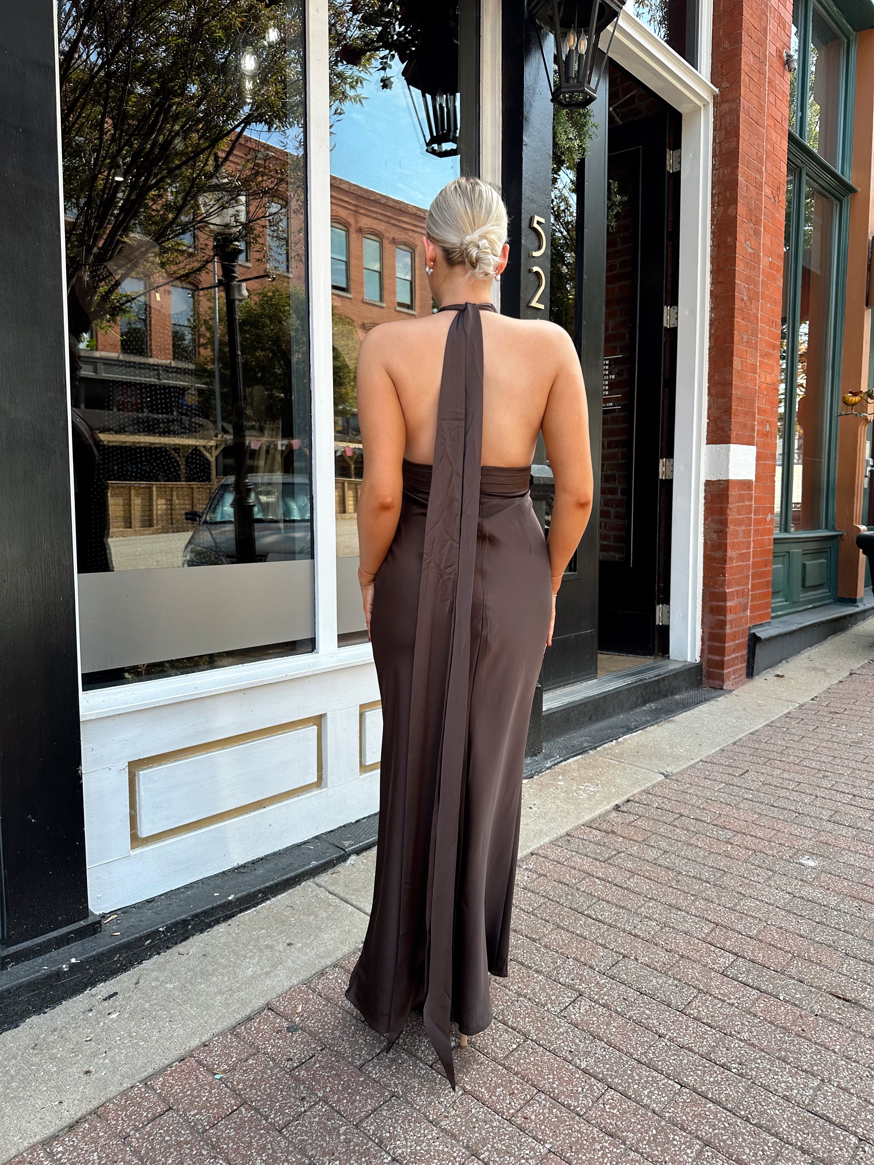 Woman wearing chocolate brown satin maxi dress with open back and long ties. 