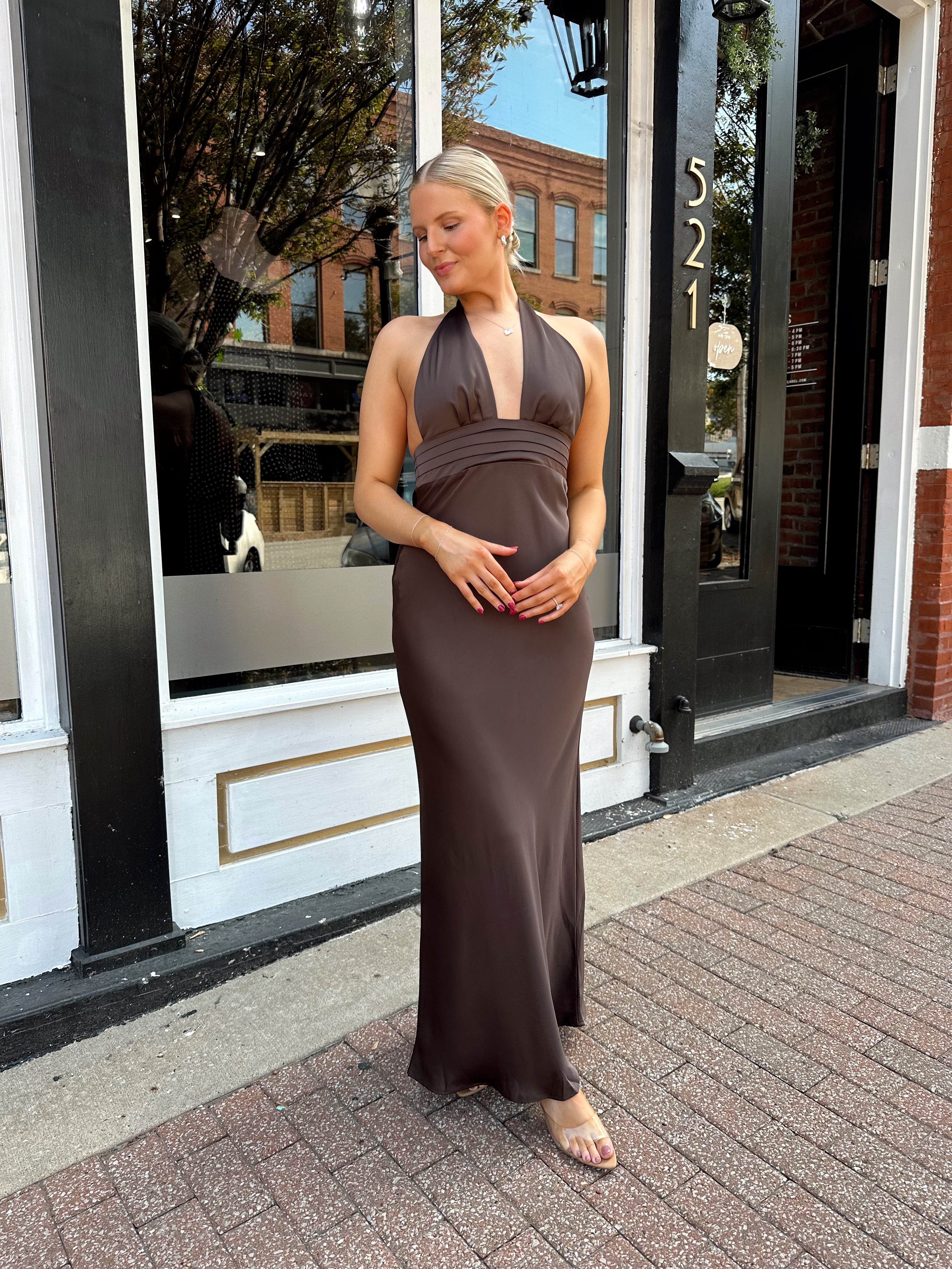 Woman wearing chocolate brown satin maxi dress with open back and long ties. 