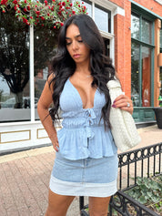 Woman wearing light wash denim mini skirt with cuffed hem and blue top. 