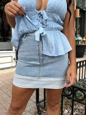 Woman wearing light wash denim mini skirt with cuffed hem and blue top. 