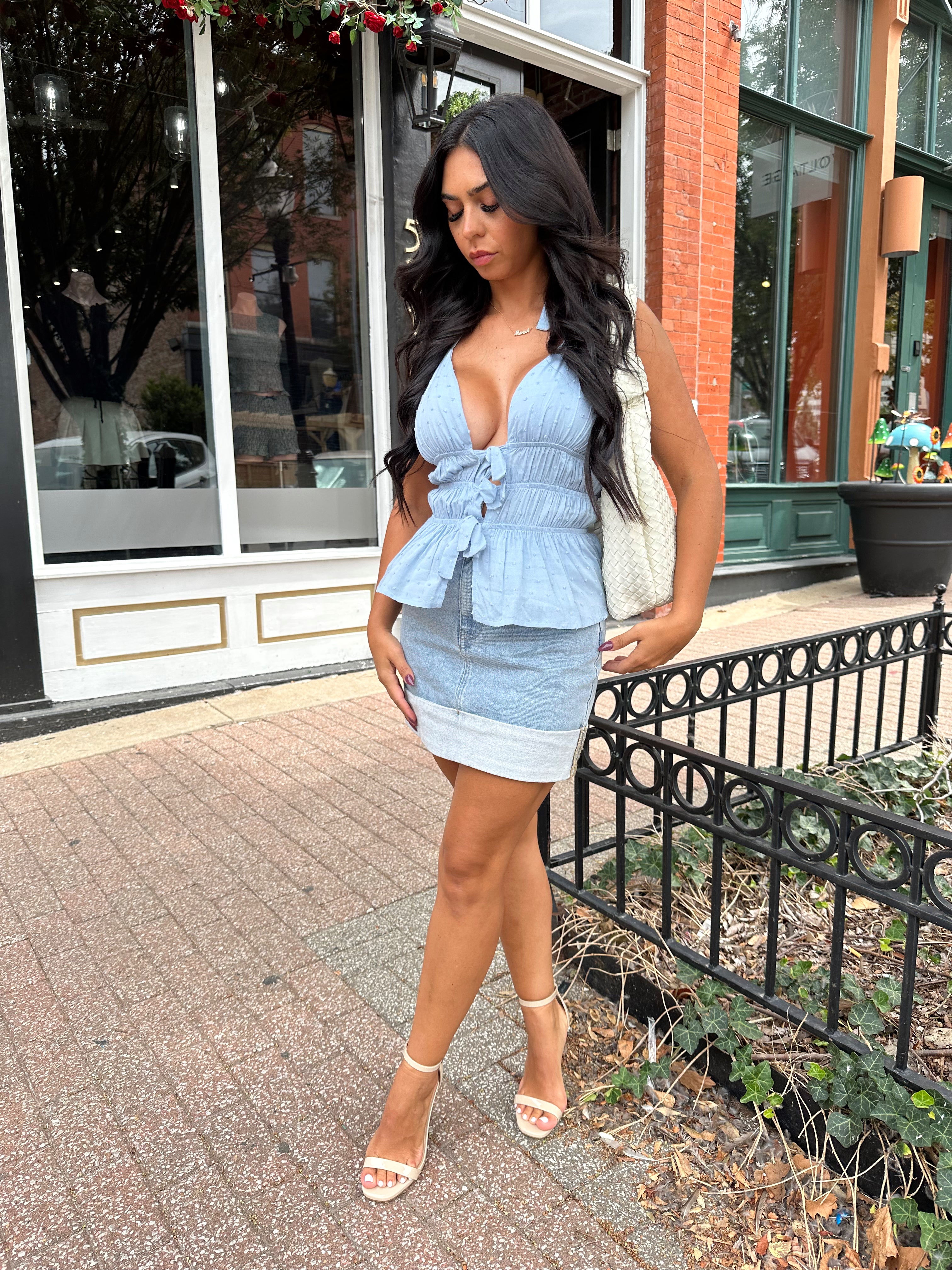 Woman wearing light wash denim mini skirt with cuffed hem and blue top. 