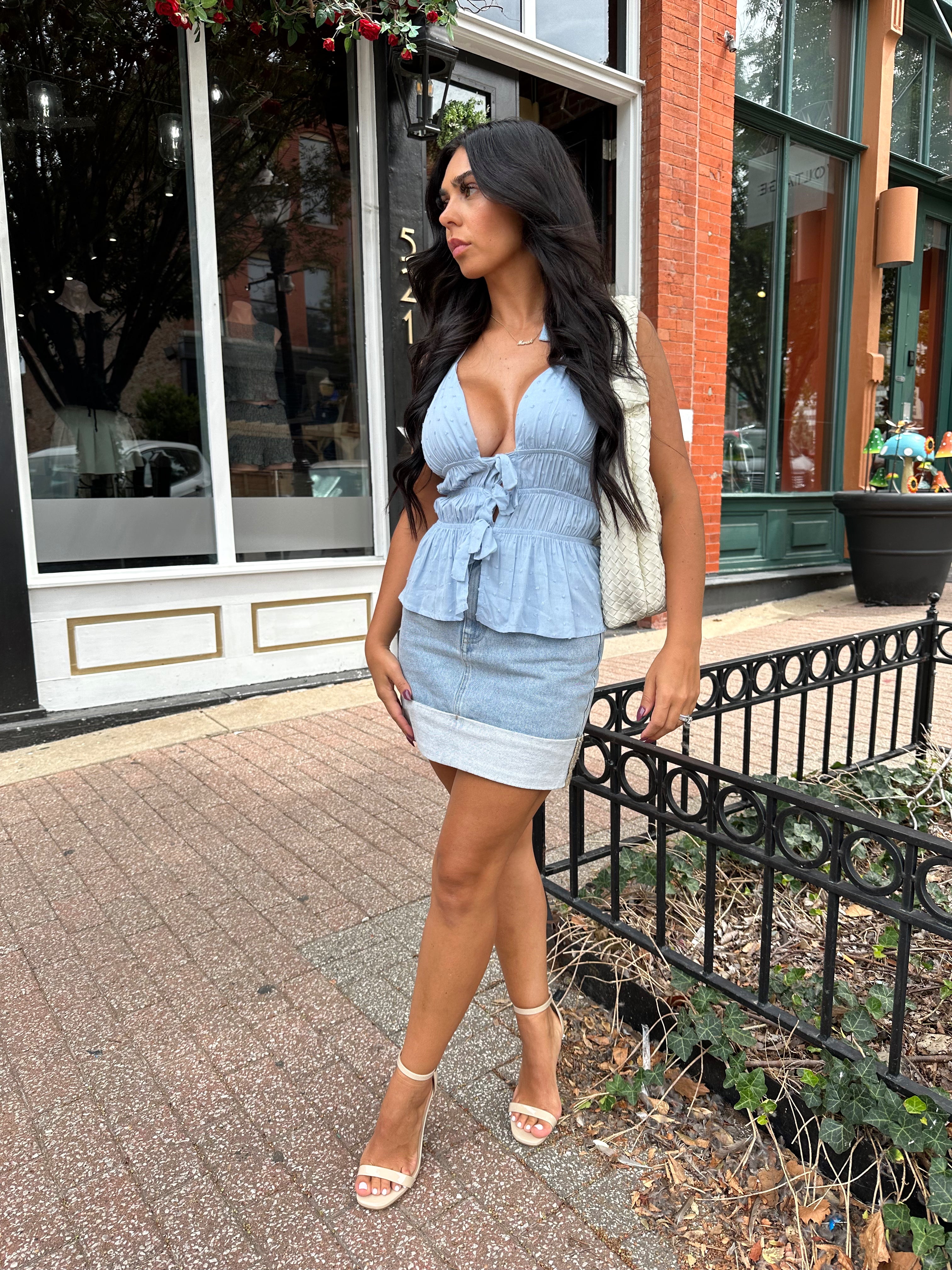 Woman wearing light wash denim mini skirt with cuffed hem and blue top. 