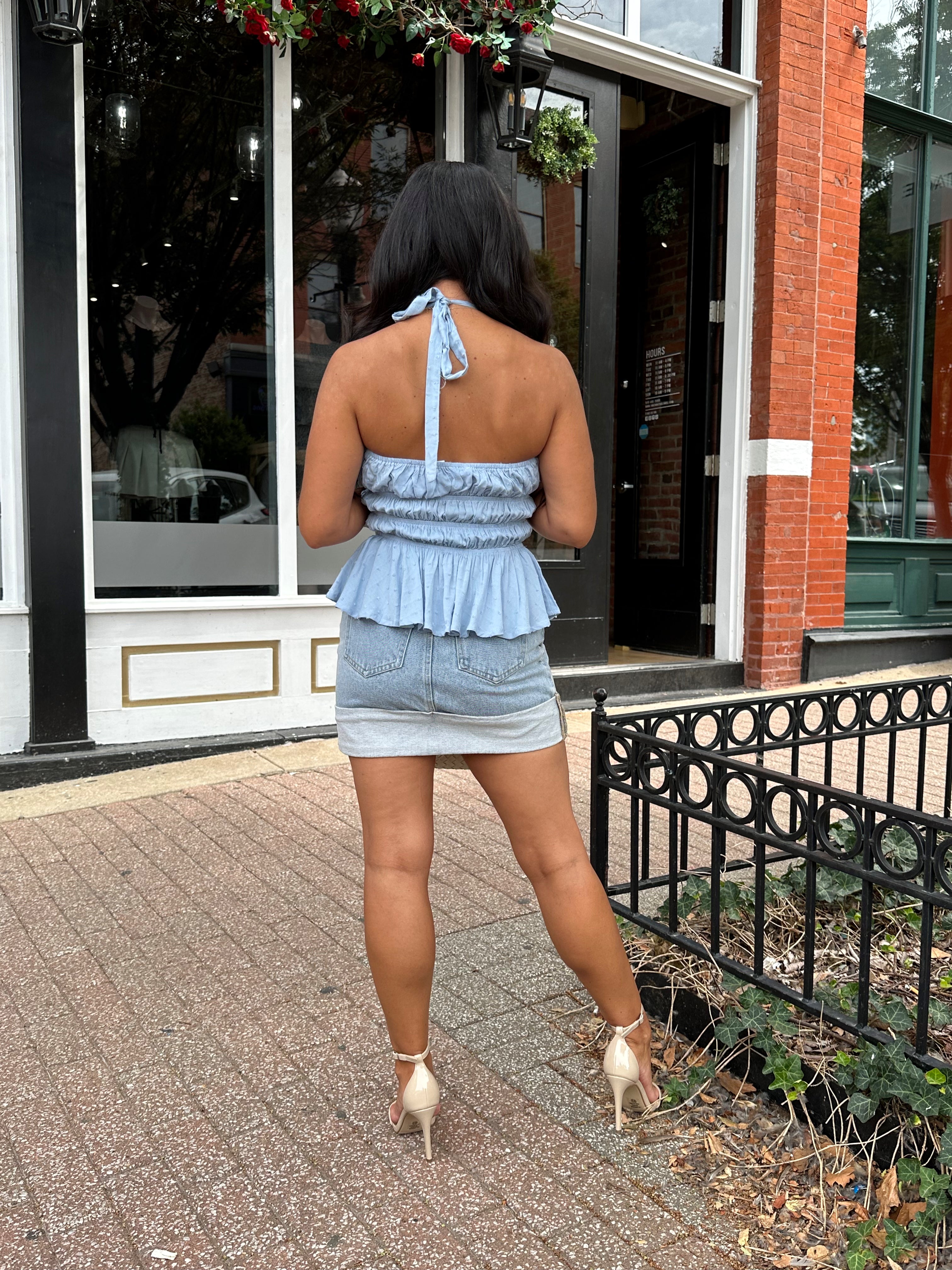 Woman wearing light wash denim mini skirt with cuffed hem and blue top. 