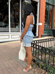 Woman wearing light wash denim mini skirt with cuffed hem and blue top. 