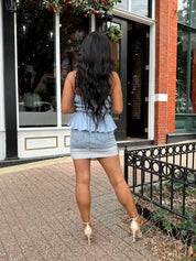Woman wearing light wash denim mini skirt with cuffed hem and blue top. 