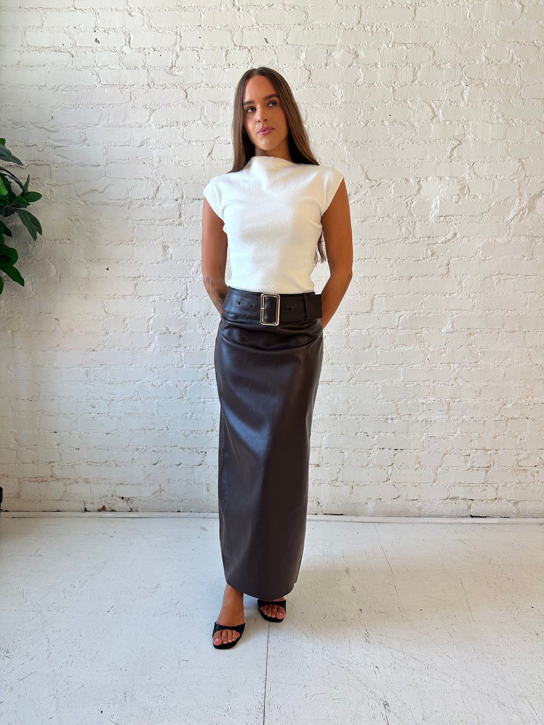 Woman wearing dark brown faux leather midi skirt with belted midsection and white cap sleeve top.