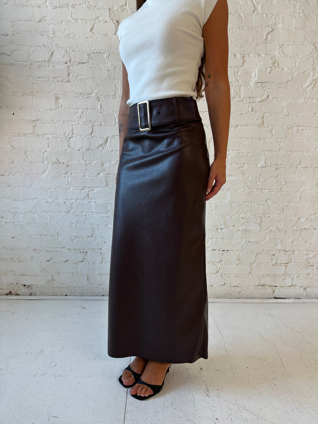Woman wearing dark brown faux leather midi skirt with belted midsection and white cap sleeve top.