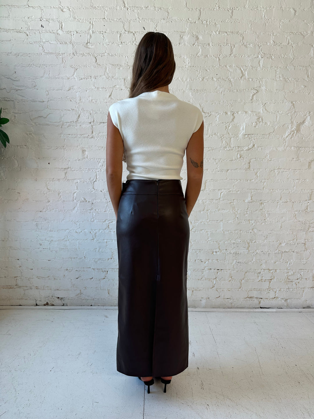 Woman wearing dark brown faux leather midi skirt with belted midsection and white cap sleeve top.
