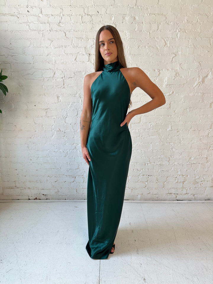 Woman wearing emerald green satin maxi dress with high self tie halter neckline. 