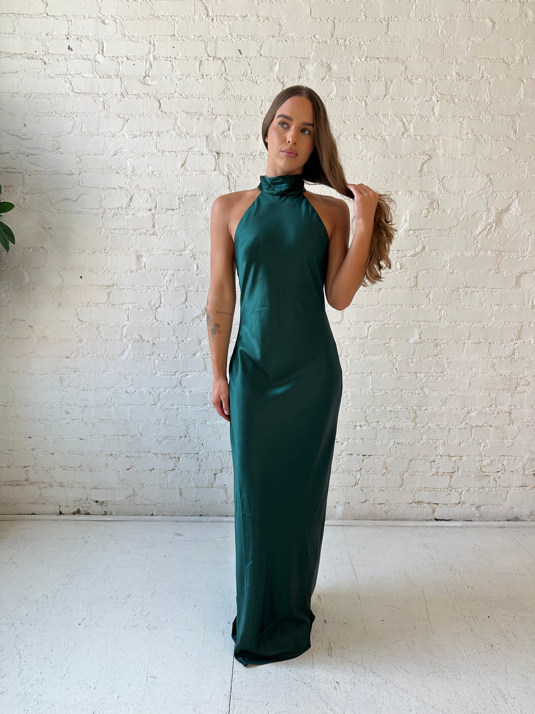 Woman wearing emerald green satin maxi dress with high self tie halter neckline. 