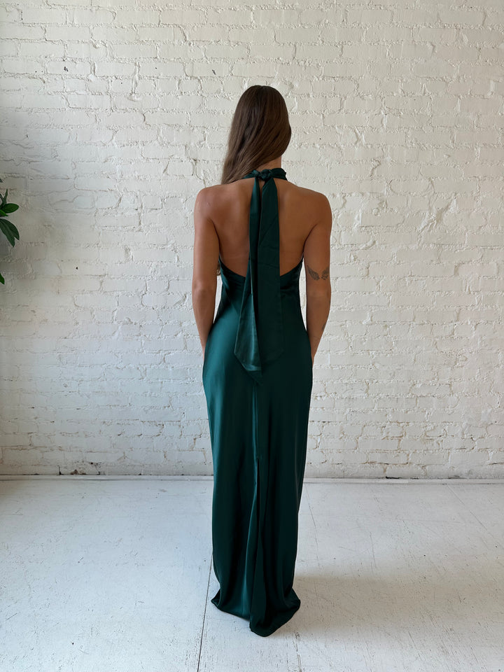 Woman wearing emerald green satin maxi dress with high self tie halter neckline. 