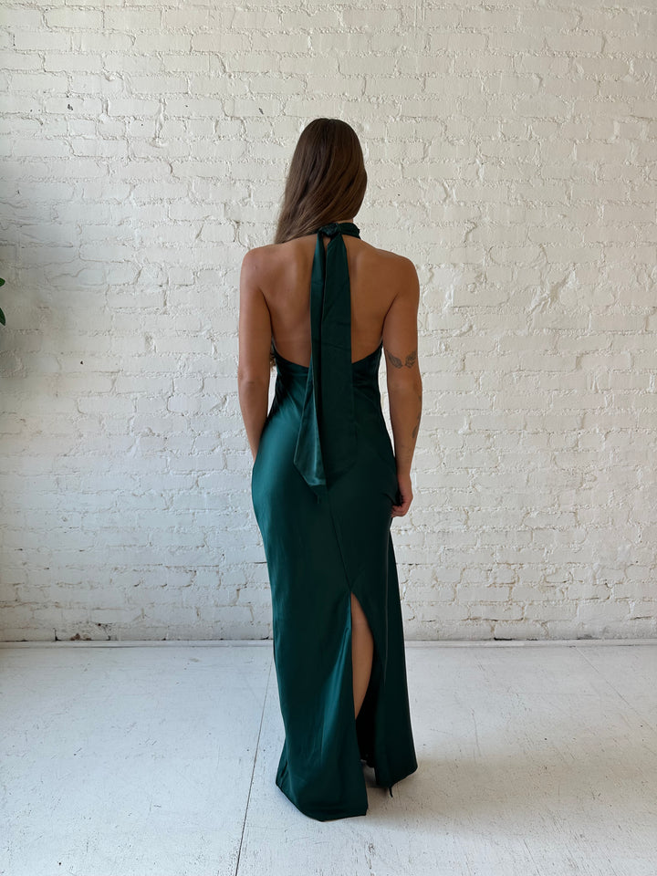 Woman wearing emerald green satin maxi dress with high self tie halter neckline. 