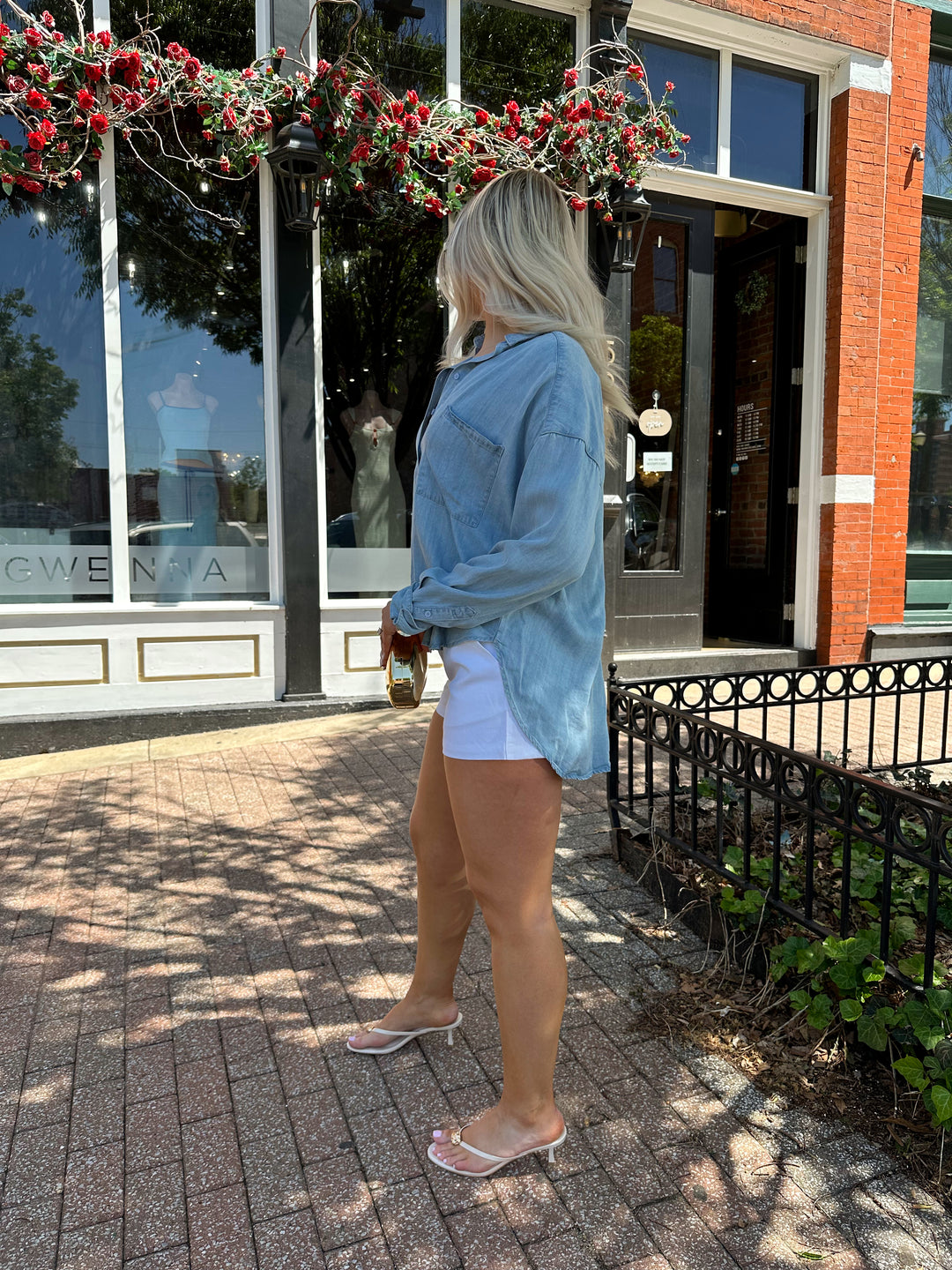 Woman wearing light wash denim chambray button down top with white micro shorts.