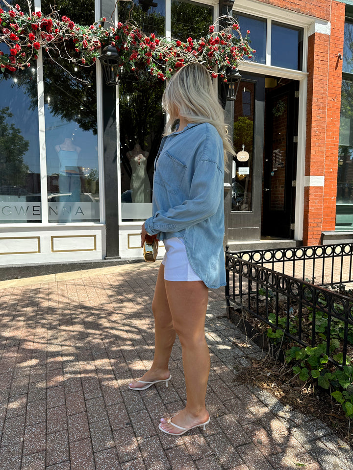 Woman wearing light wash denim chambray button down top with white micro shorts.