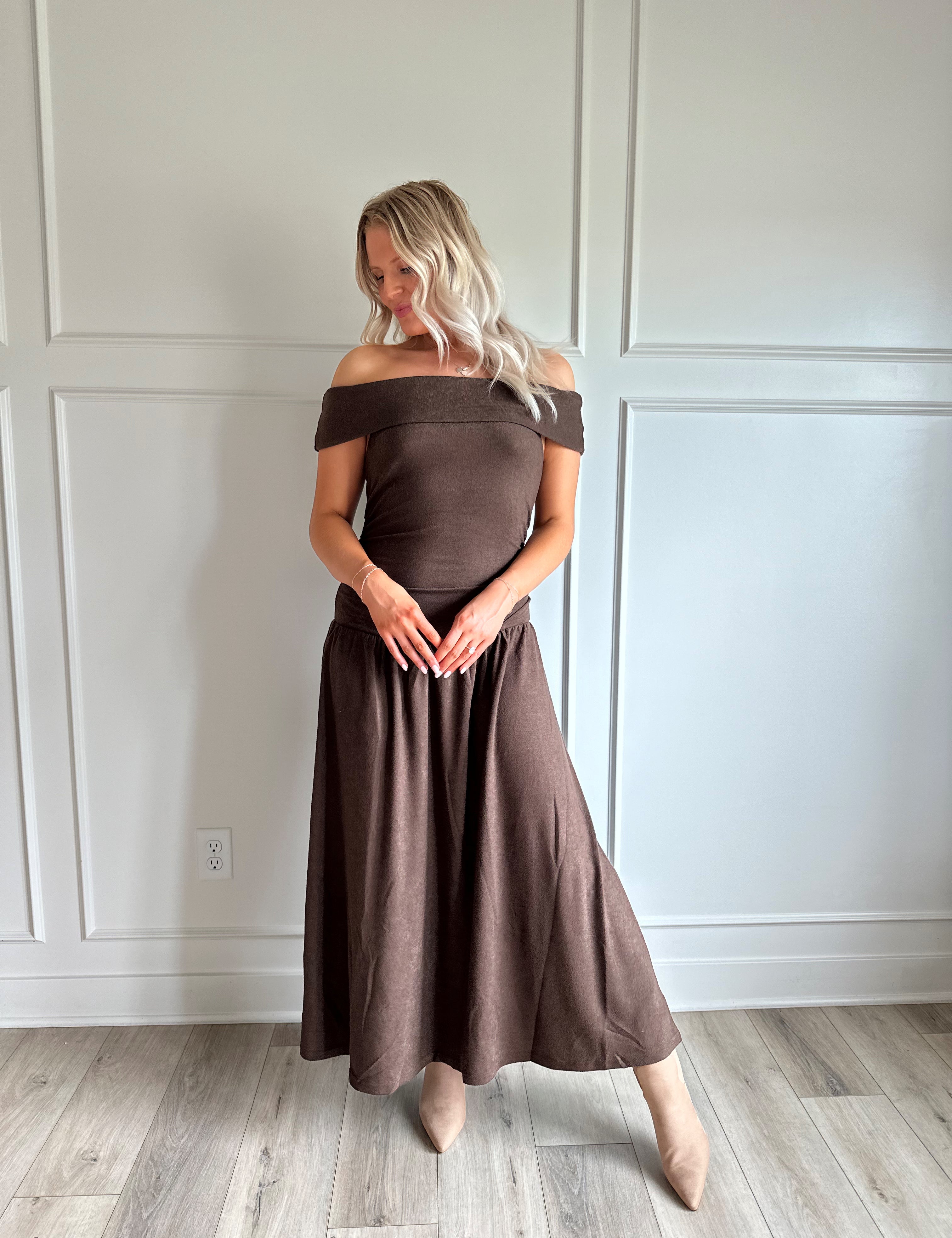 Woman wearing brown off the shoulder midi dress with drop waist and sheen. 