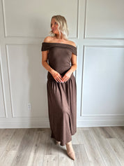 Woman wearing brown off the shoulder midi dress with drop waist and sheen. 