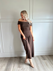 Woman wearing brown off the shoulder midi dress with drop waist and sheen. 
