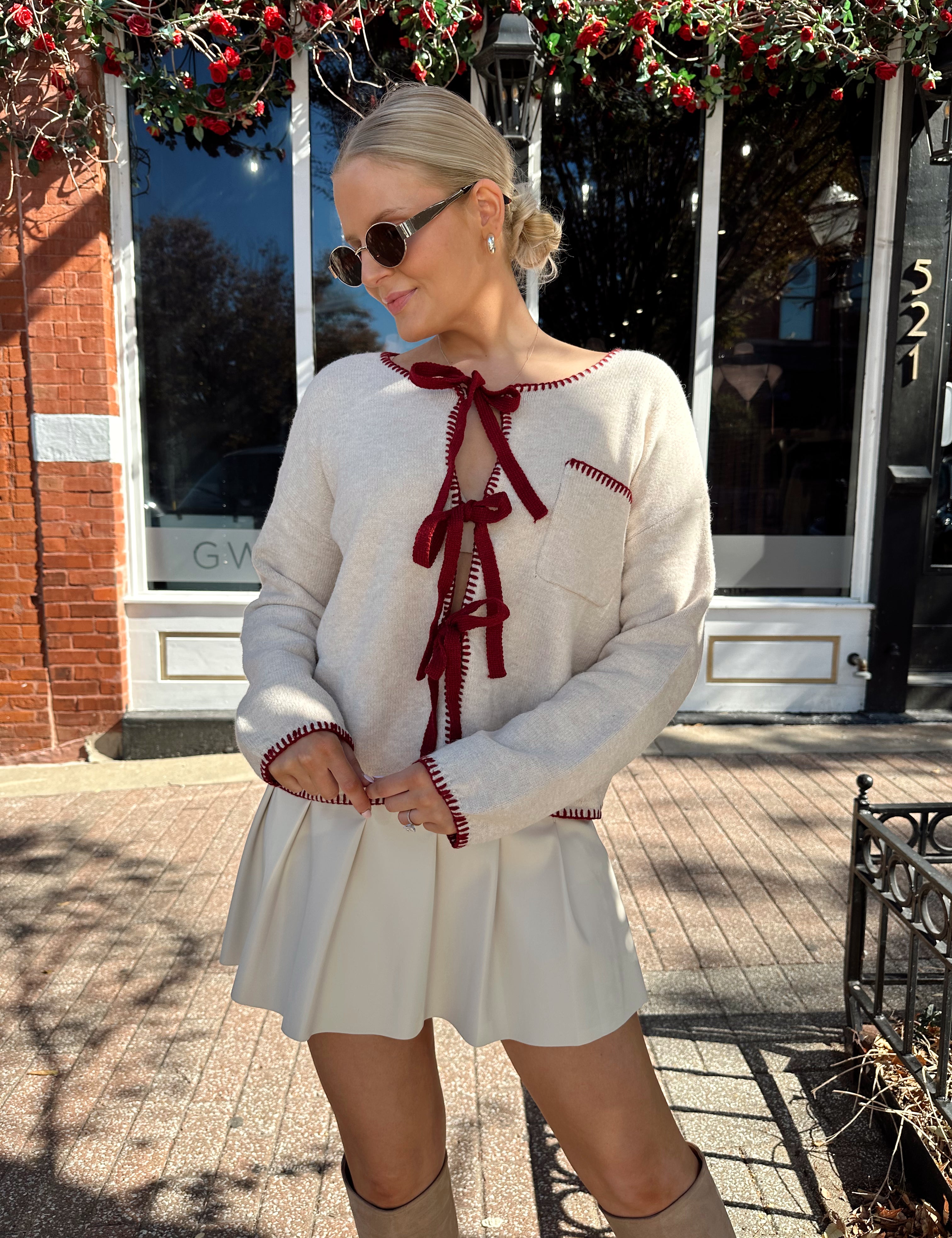 Woman wearing cream front tie cardigan with burgundy stitch detailing. 