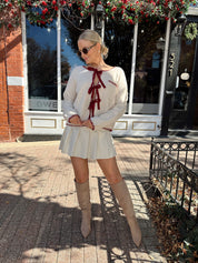 Woman wearing cream front tie cardigan with burgundy stitch detailing. 