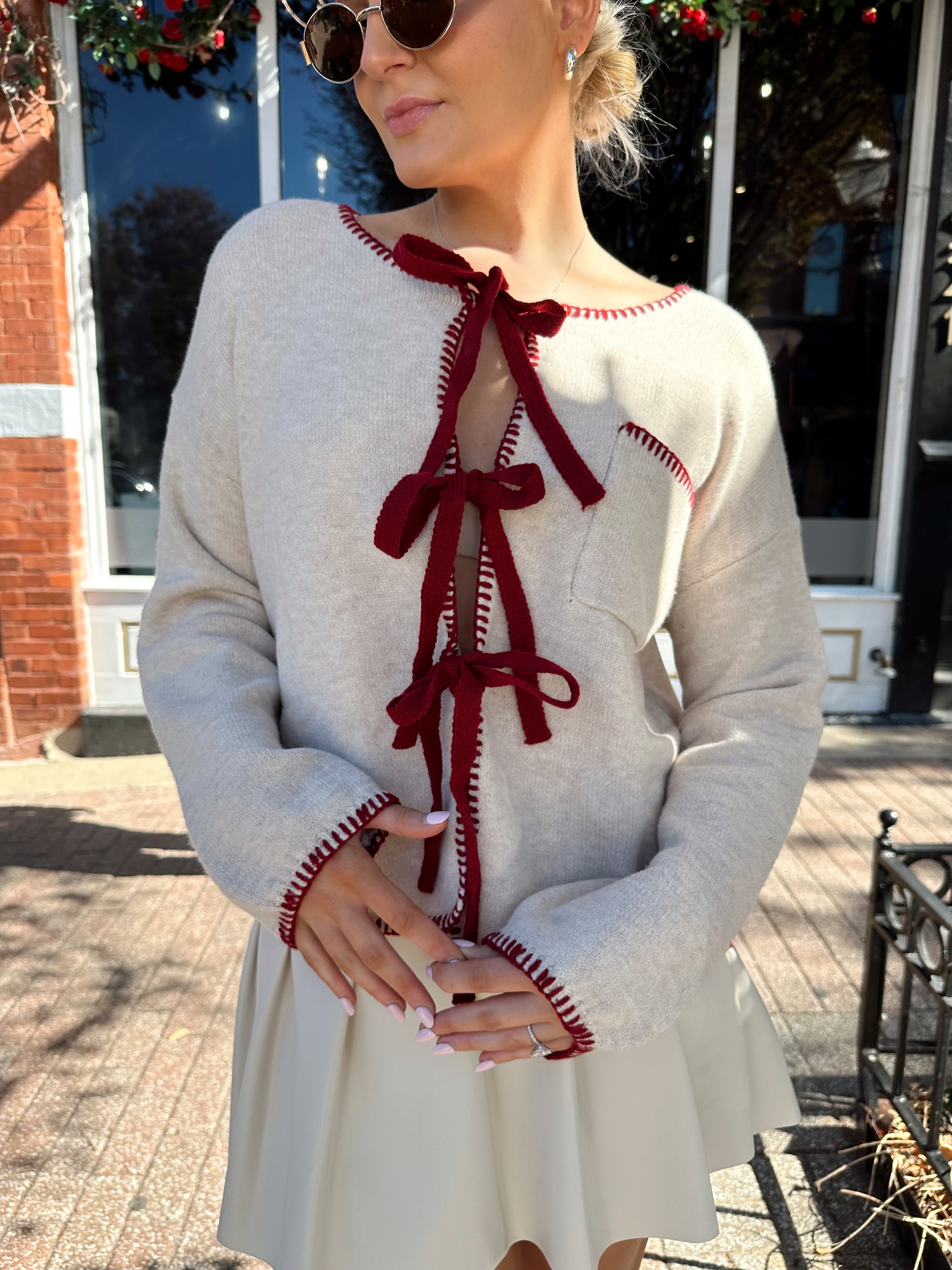 Woman wearing cream front tie cardigan with burgundy stitch detailing. 