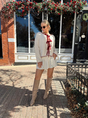 Woman wearing cream front tie cardigan with burgundy stitch detailing. 