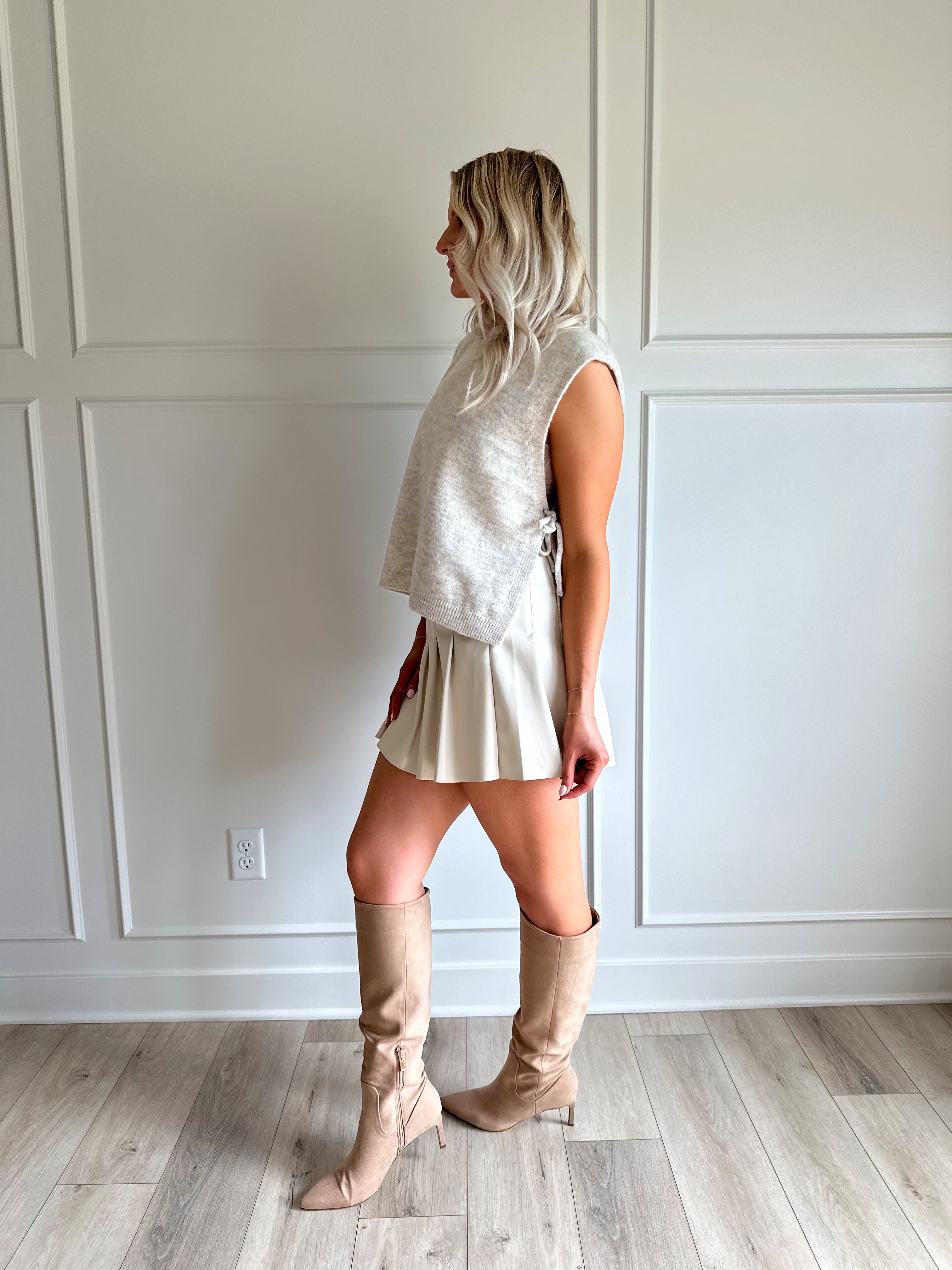 Woman wearing a cream vegan leather pleated mini skirt and oatmeal knit sleeveless top. 