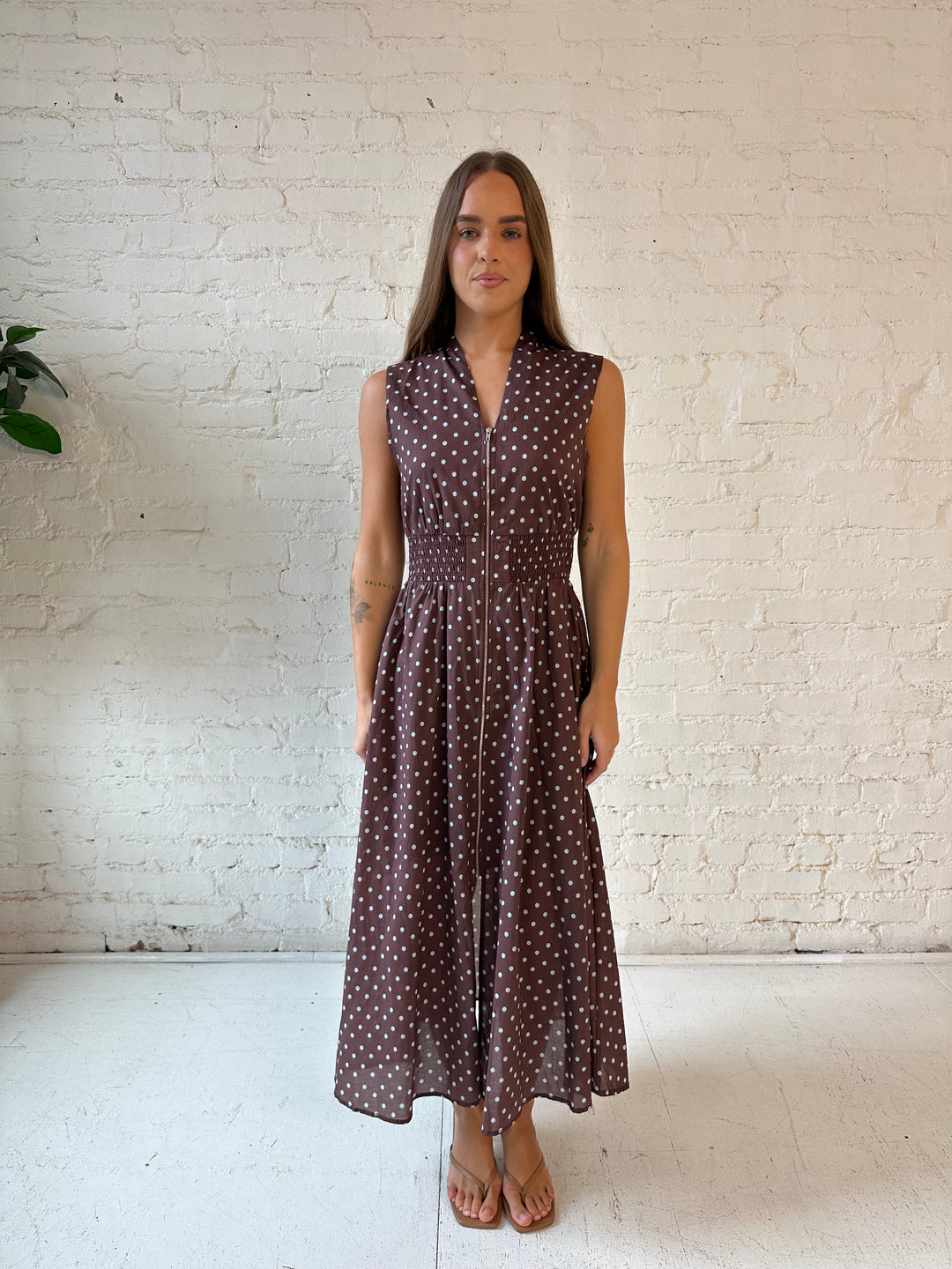 Woman wearing brown polka dot midi dress with smocked midsection and front zipper closure. 