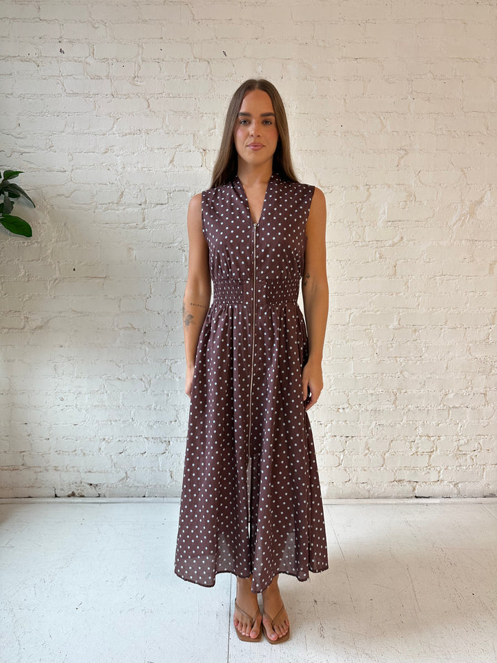 Woman wearing brown polka dot midi dress with smocked midsection and front zipper closure. 