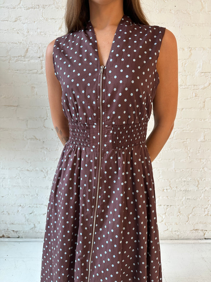 Woman wearing brown polka dot midi dress with smocked midsection and front zipper closure. 