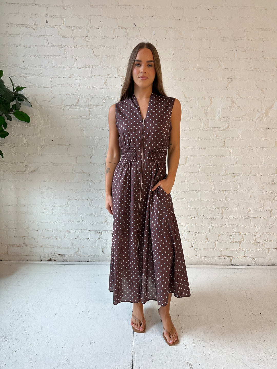 Woman wearing brown polka dot midi dress with smocked midsection and front zipper closure. 