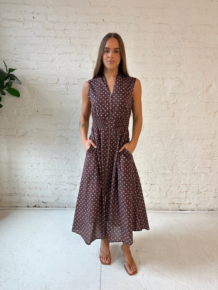 Woman wearing brown polka dot midi dress with smocked midsection and front zipper closure. 