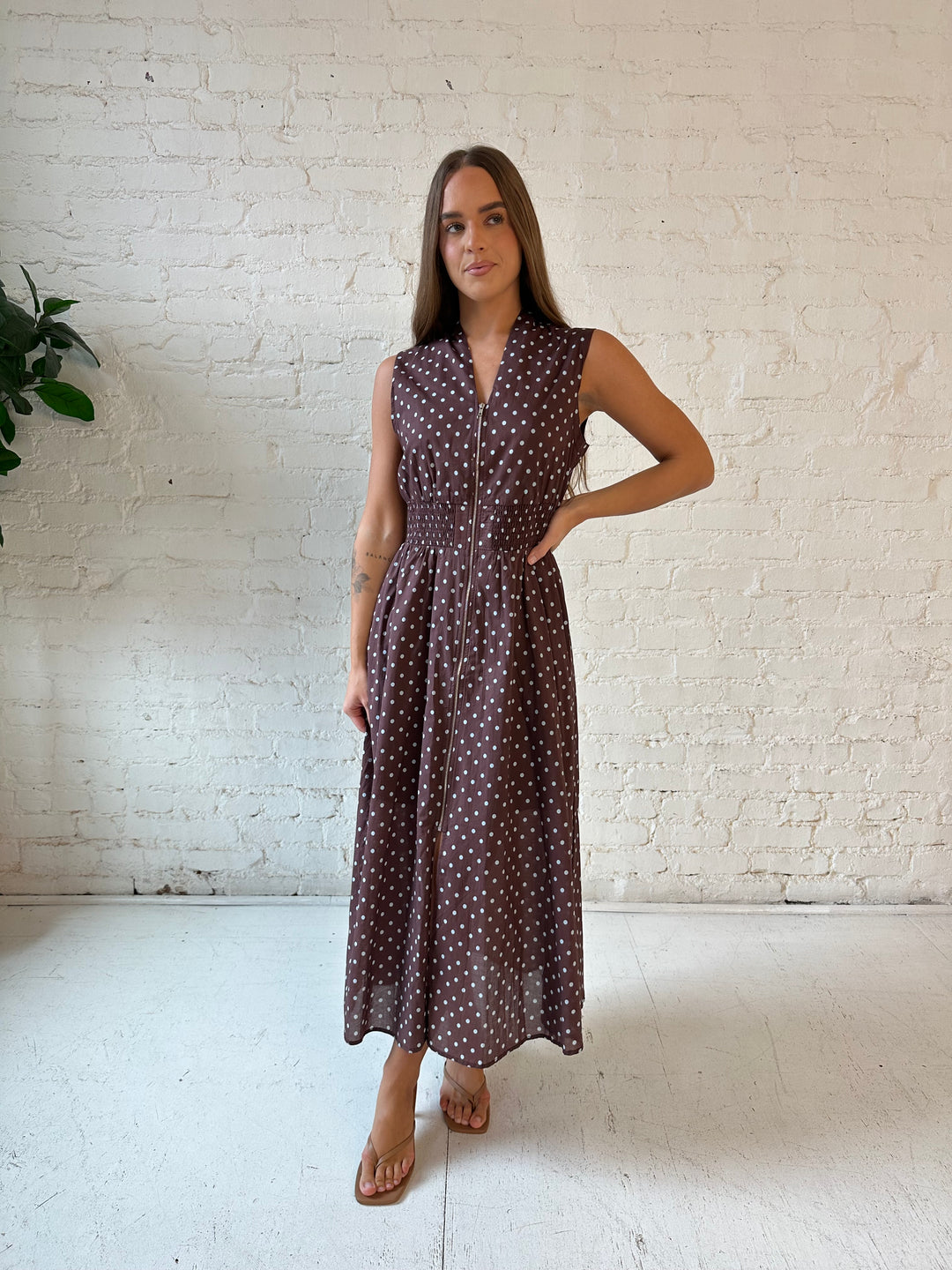 Woman wearing brown polka dot midi dress with smocked midsection and front zipper closure. 