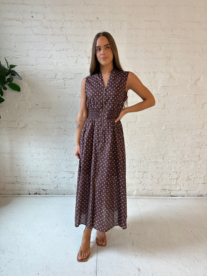 Woman wearing brown polka dot midi dress with smocked midsection and front zipper closure. 