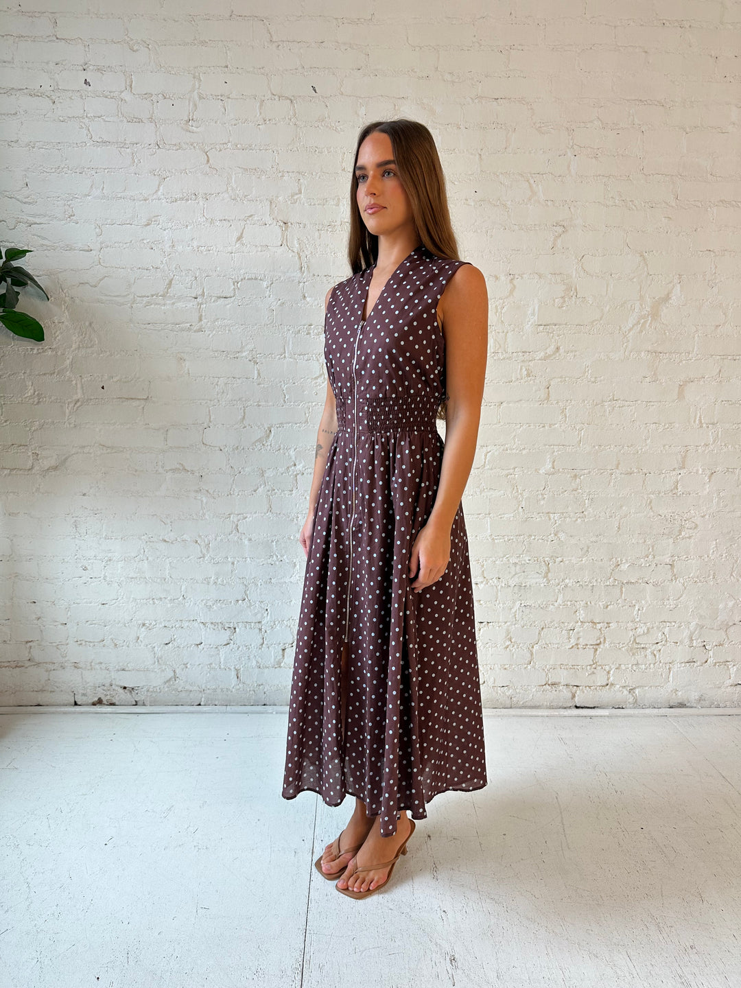 Woman wearing brown polka dot midi dress with smocked midsection and front zipper closure. 
