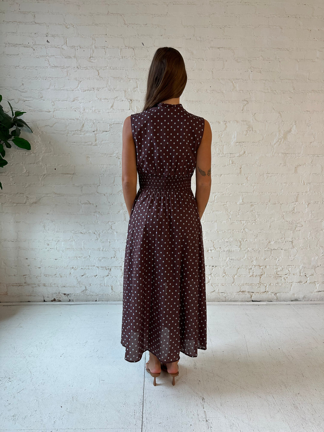 Woman wearing brown polka dot midi dress with smocked midsection and front zipper closure. 