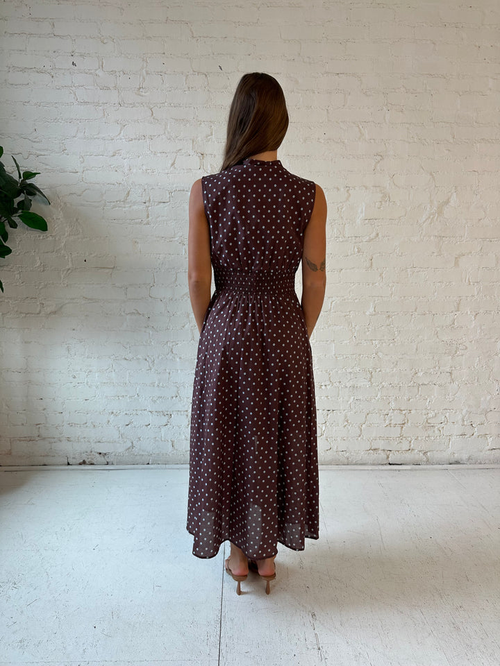 Woman wearing brown polka dot midi dress with smocked midsection and front zipper closure. 