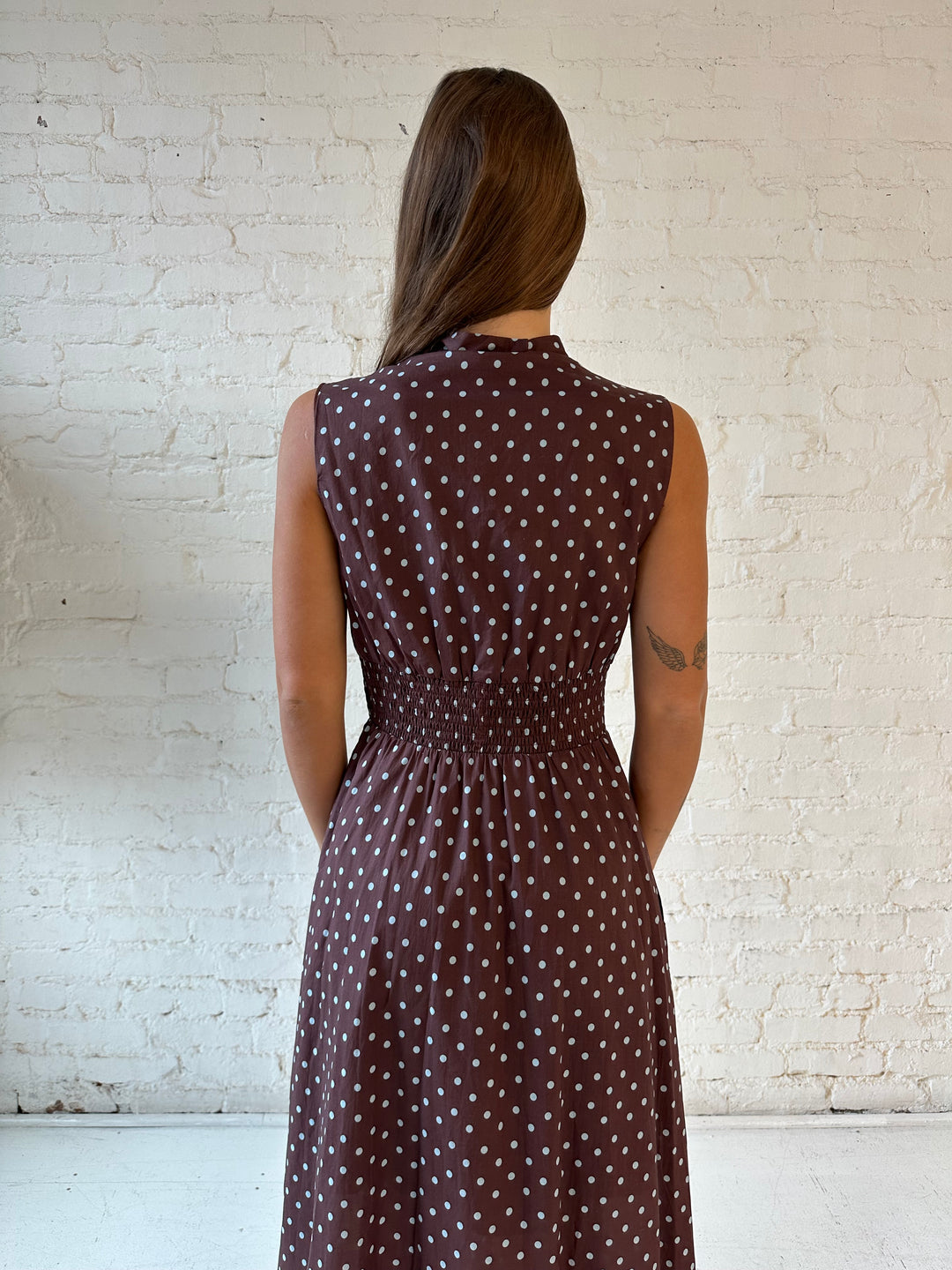 Woman wearing brown polka dot midi dress with smocked midsection and front zipper closure. 