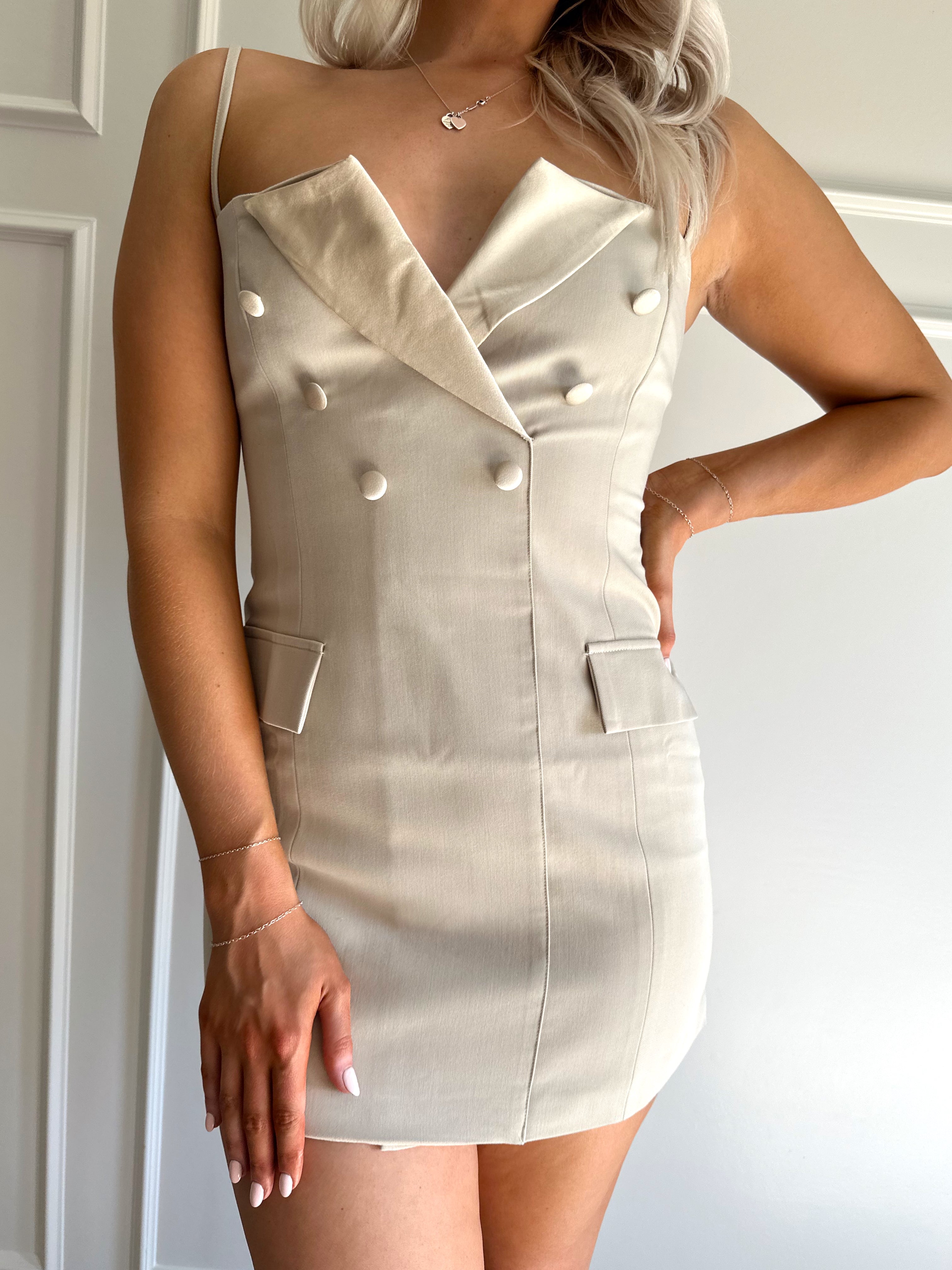 Woman wearing a beige tailored mini dress with satin collar and button detailing.
