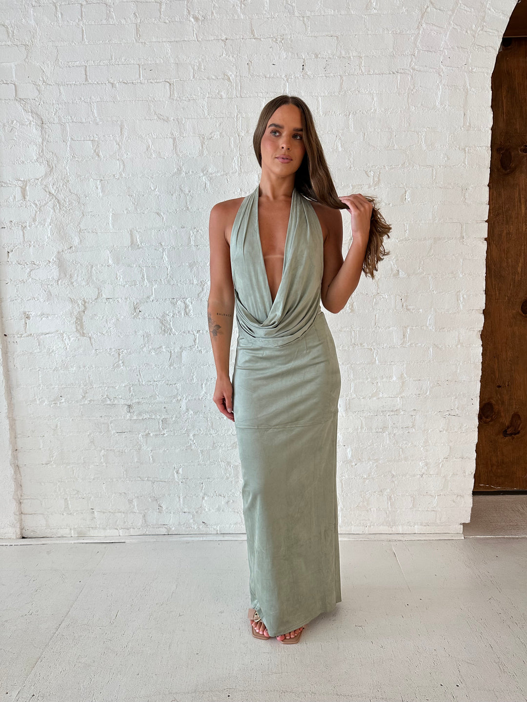 Woman wearing sage green faux suede two piece set with halter plunging cowl top, and maxi skirt. 