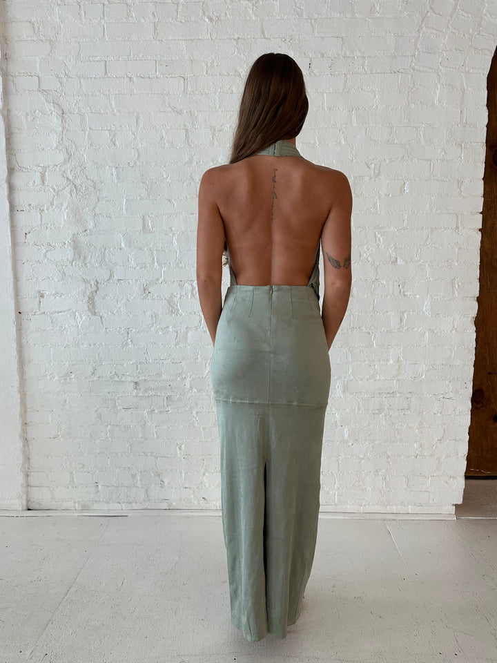 Woman wearing sage green faux suede two piece set with halter plunging cowl top, and maxi skirt. 
