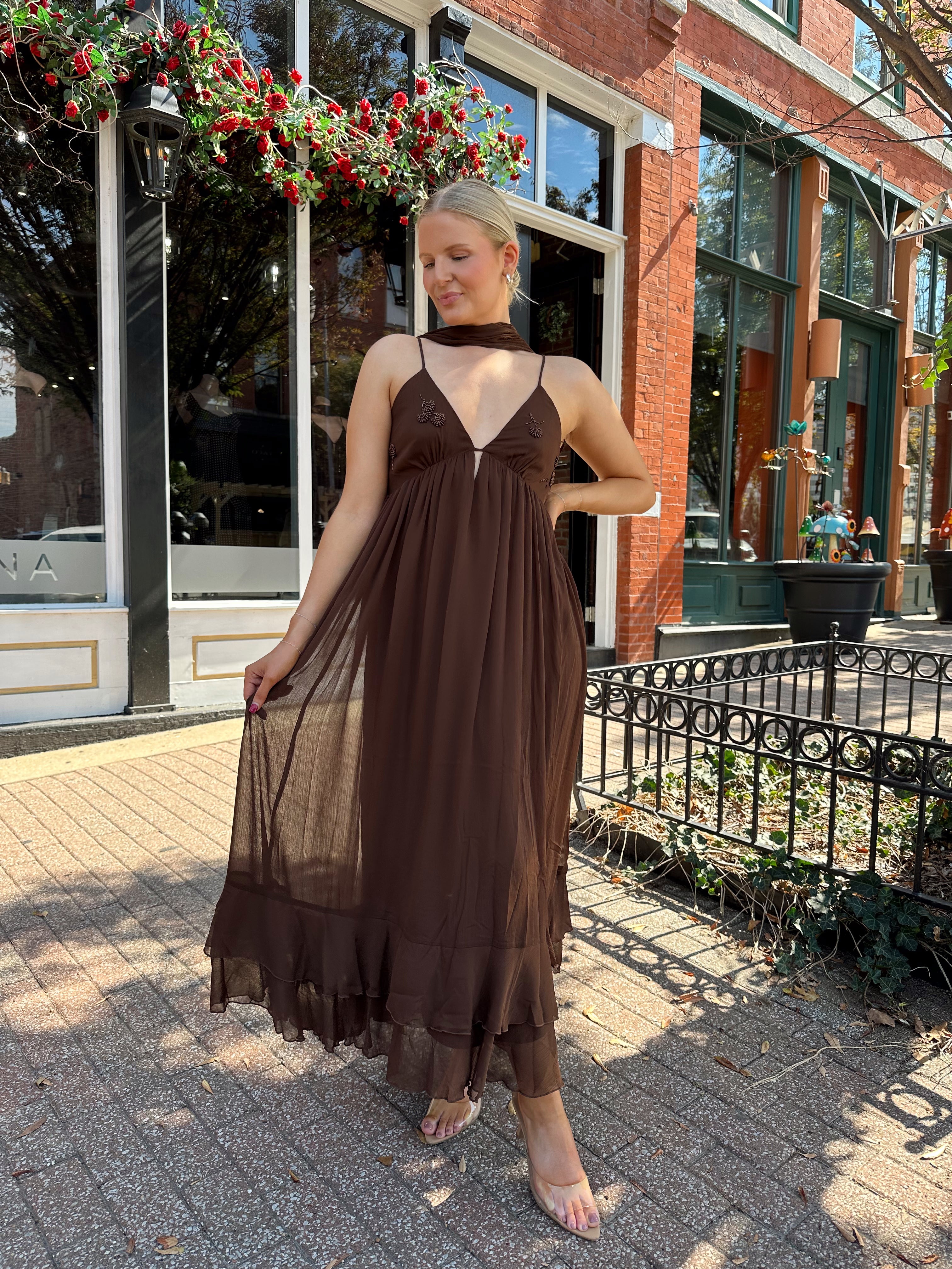 Woman wearing brown maxi dress with beaded detailing and detachable neck scarf.