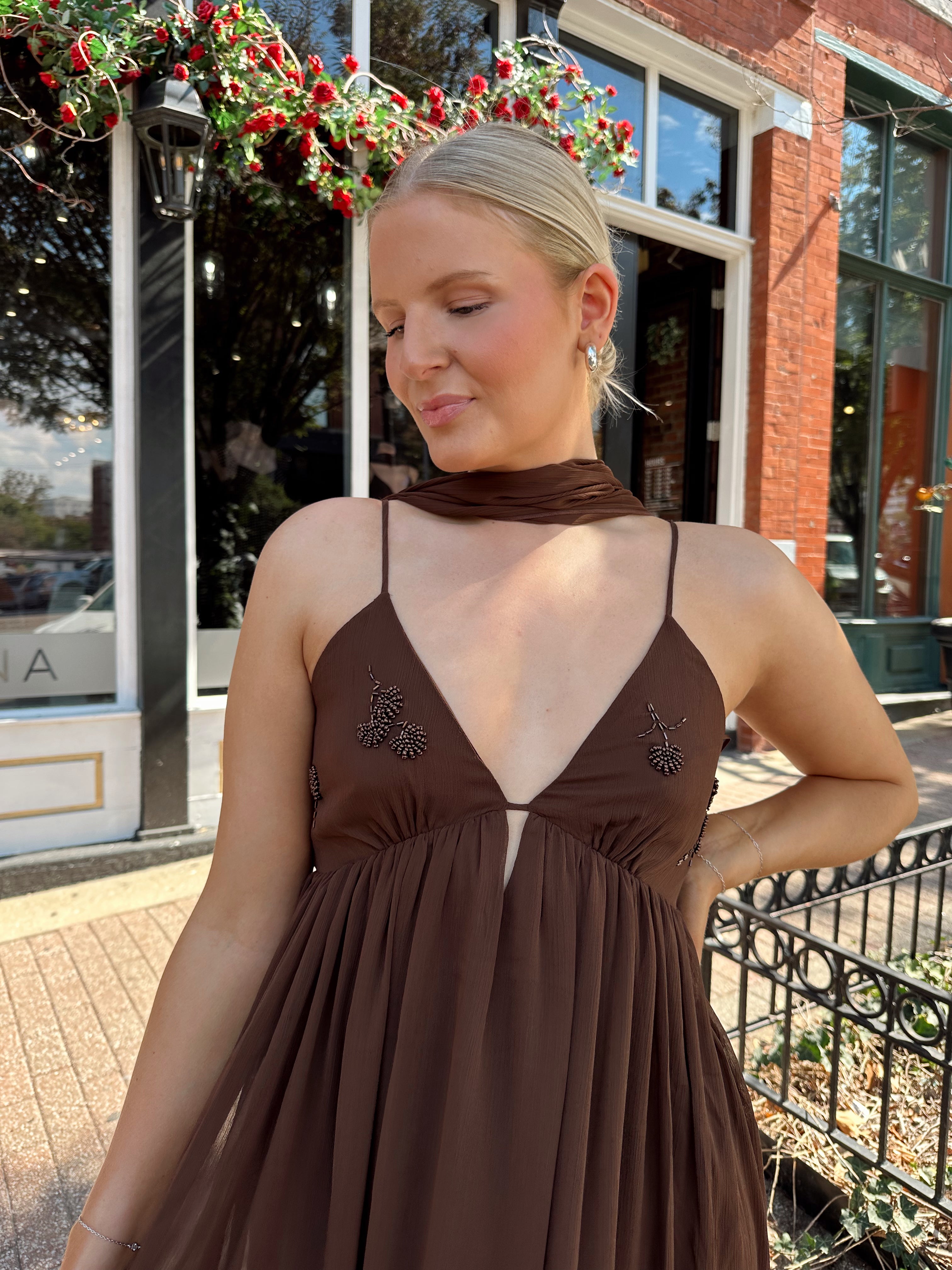 Woman wearing brown maxi dress with beaded detailing and detachable neck scarf.